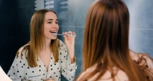 woman brushing her teeth in front of a mirror